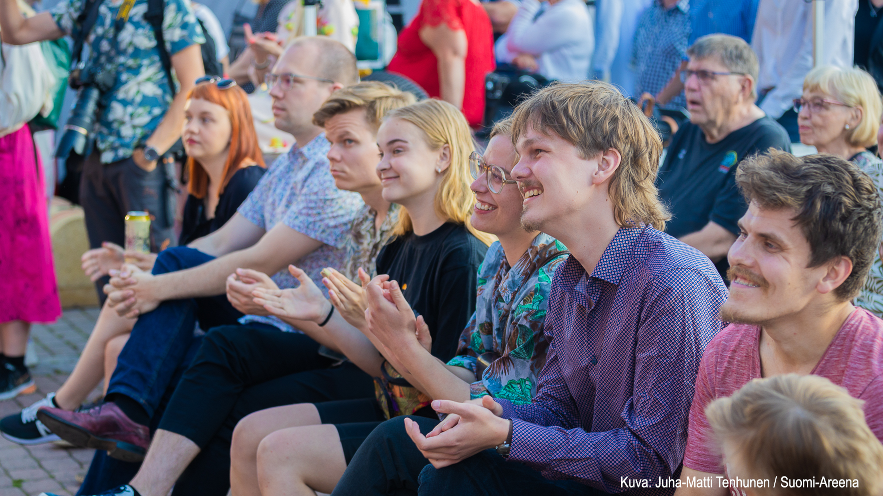 Yleisöä SuomiAreenassa kuuntelemassa kiinnostuneena ja hymyilevinä.