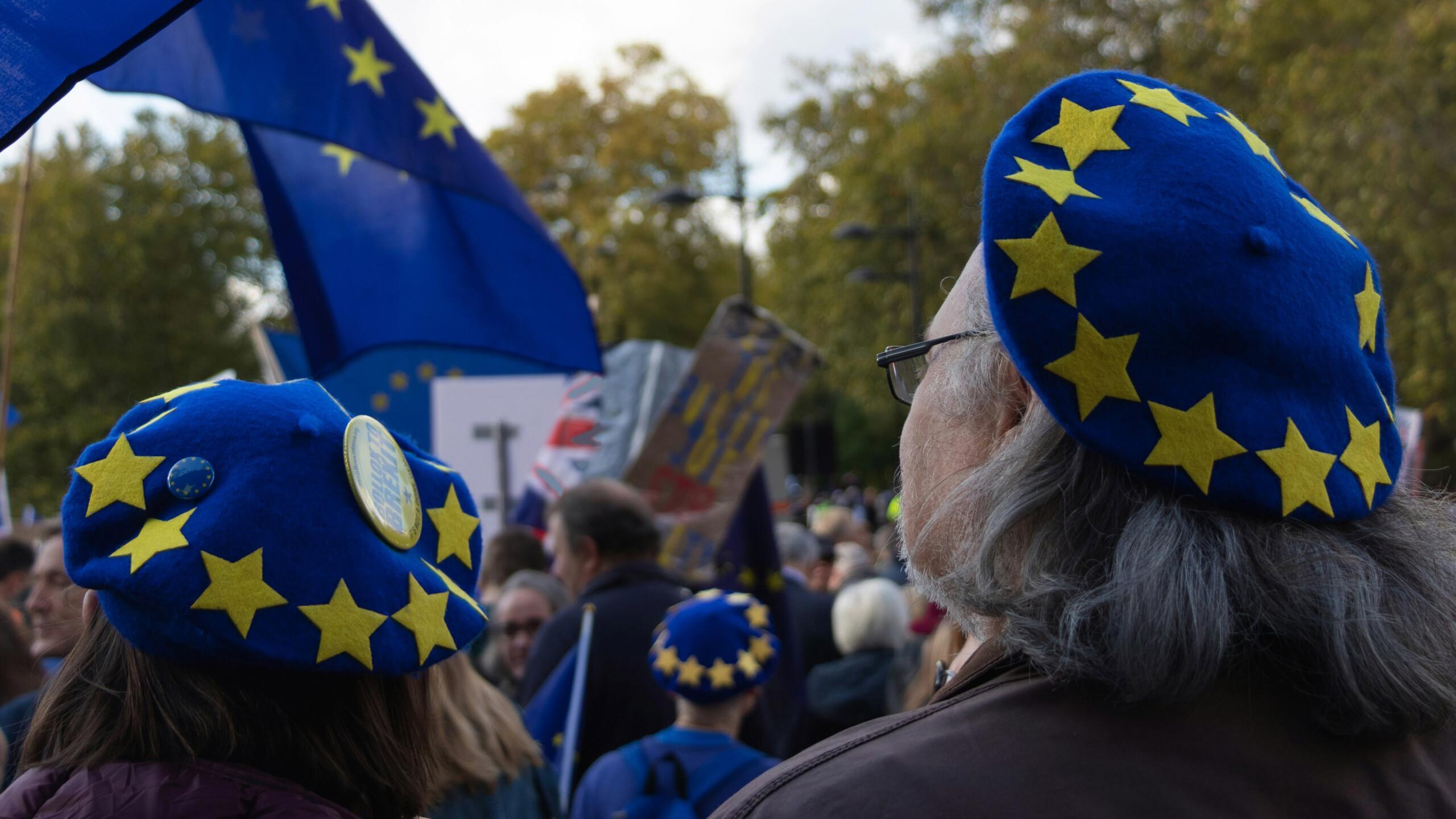 Mielenosoittajia mielenosoituksessa EU-tähdin koristelluissa sinisissä baskereissa ja EU-lipun kanssa.