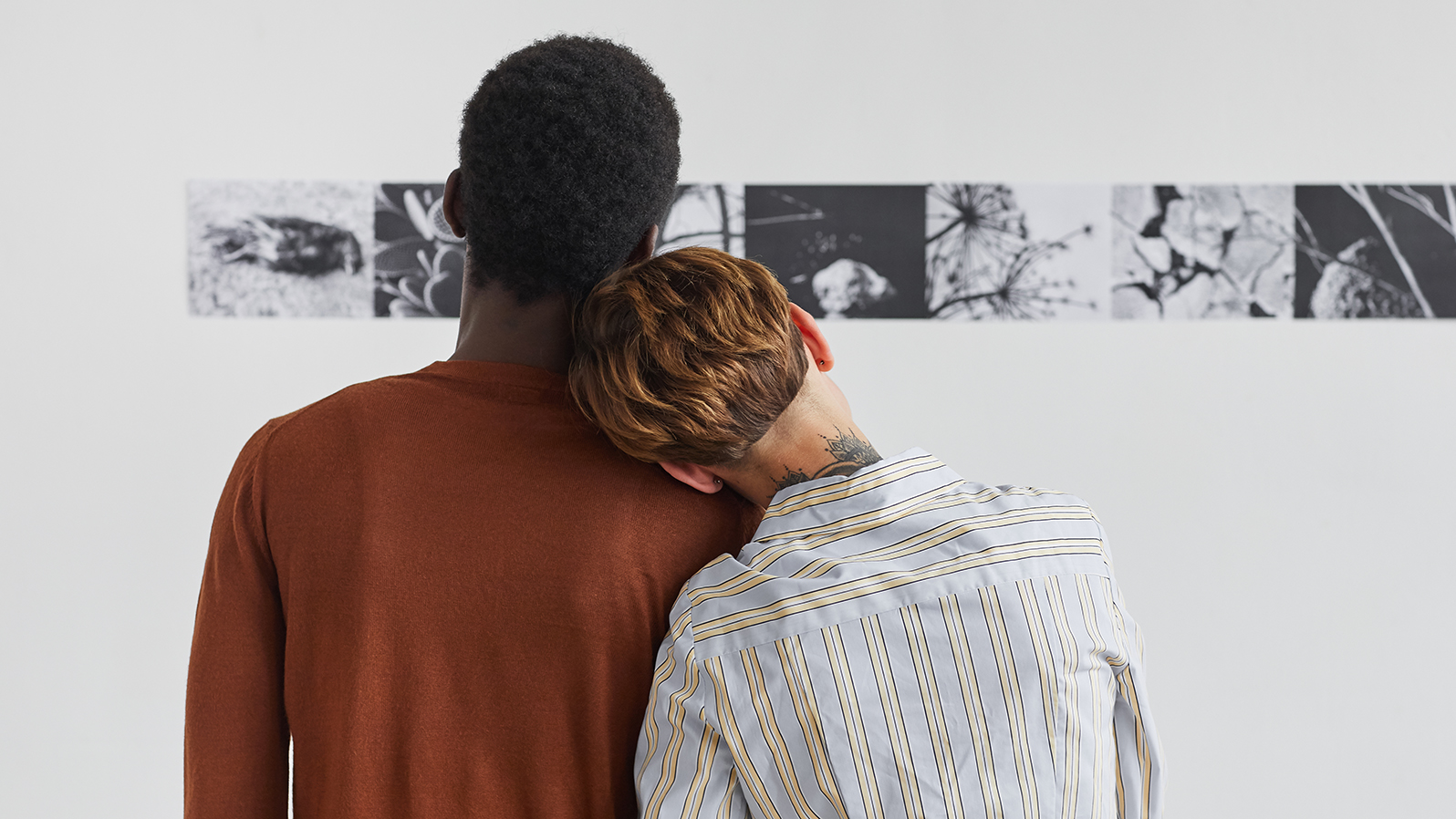 Back view portrait of mixed-race couple embracing while looking at paintings at modern art gallery exhibition, copy space